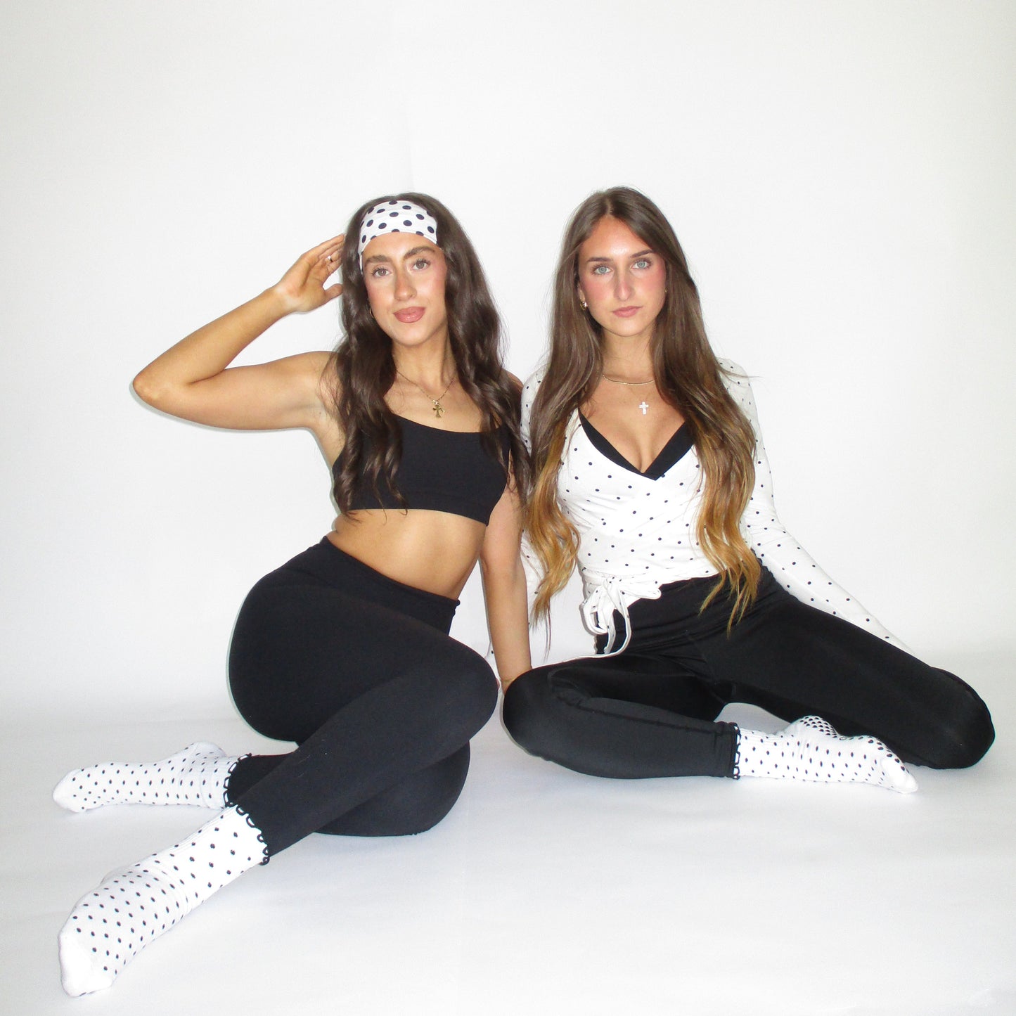 Two people in matching black outfits with white polka dots on a white background