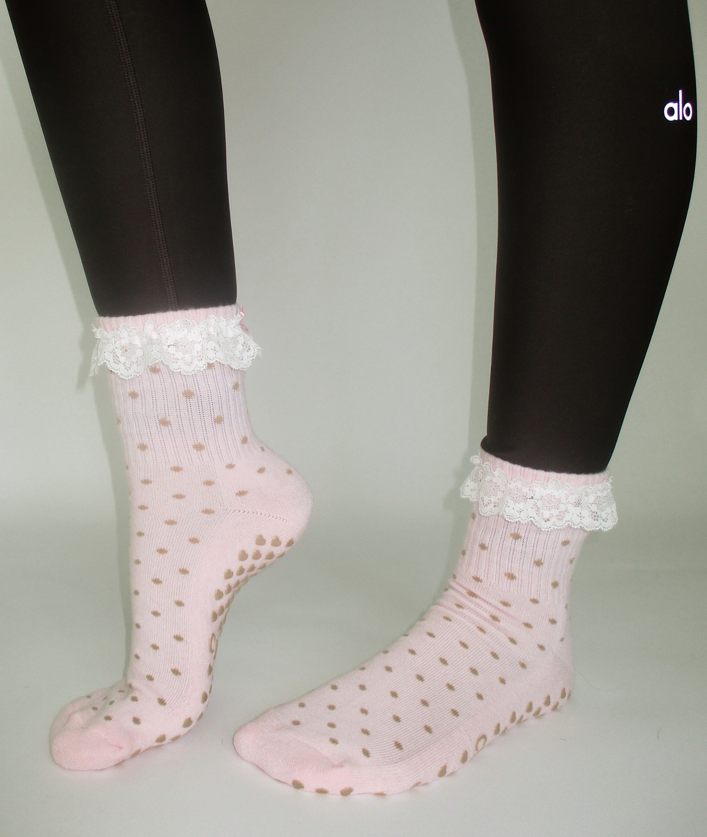 Pink socks with white lace trim worn with black leggings on a neutral background