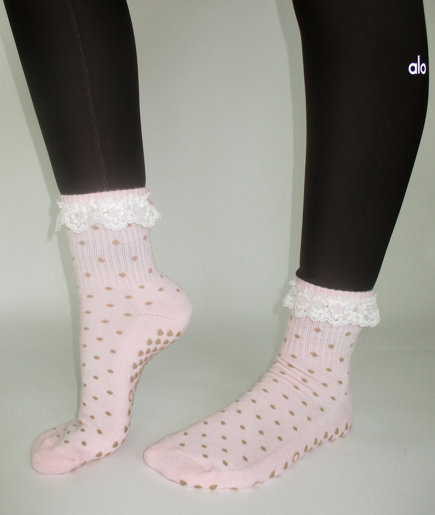Pink socks with white lace trim worn with black leggings on a neutral background